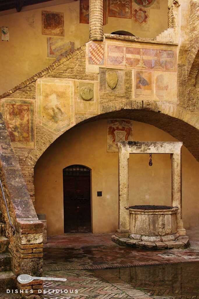 Foto vom Innenhof des Palazzo Comunale mit einem zentralen Brunnen und einer freskenverzierten Treppe, die an der Seite in die Höhe führt.
