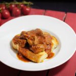 Foto von Buglione, Lammfleisch mit Sauce auf einer Brotscheibe in einem tiefen Teller serviert.