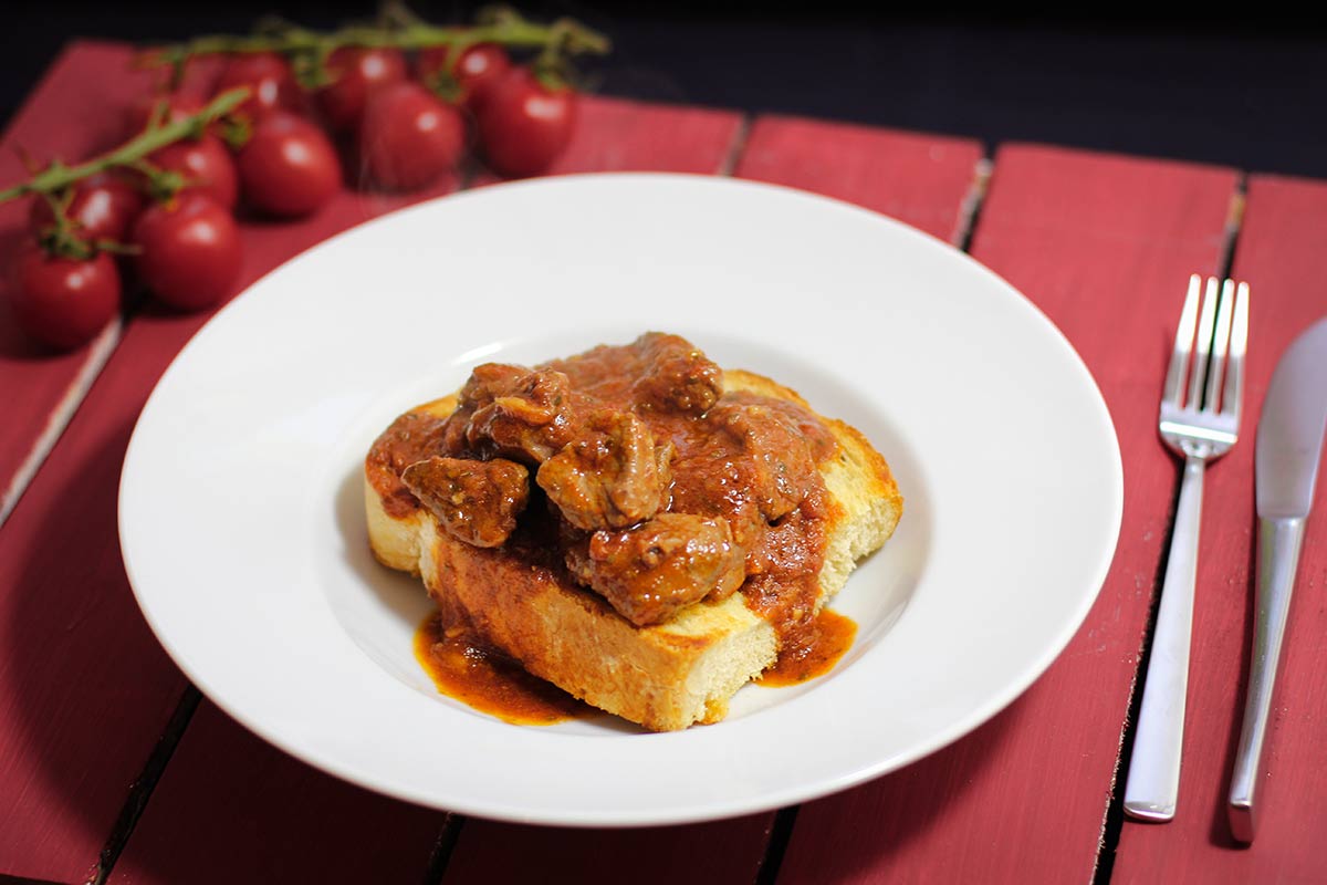 Foto von Buglione, Lammfleisch mit Sauce auf einer Brotscheibe in einem tiefen Teller serviert.