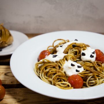 Ein Teller Spaghetti mit schwarzem Knoblauch, Tomaten und Burrata