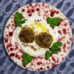 Ein Teller mit zwei Kofta-Fischfrikadellen auf Joghurtsauce