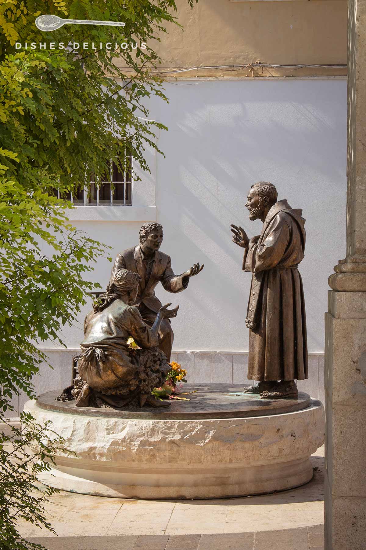 Skulptur mit Metallfiguren: zwei Menschen bitten um den Segen eines Mönchs.