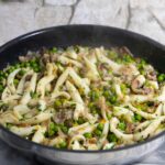 Eine Pfanne mit kleingeschnittenen Sepien mit Erbsen und Pancetta.