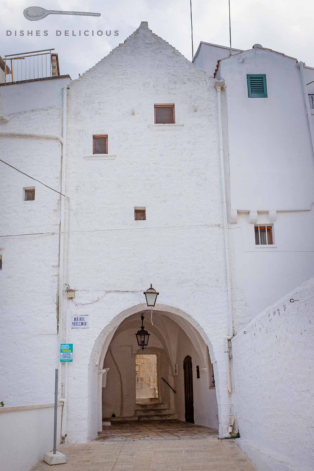 Weißgetünchtes Haus mit einem Torbogen, der in die Altstadt von Cisternino führt.