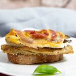 Eine Brotscheibe belegt mit einer gegrillten Sardine, Käse und Pancetta.