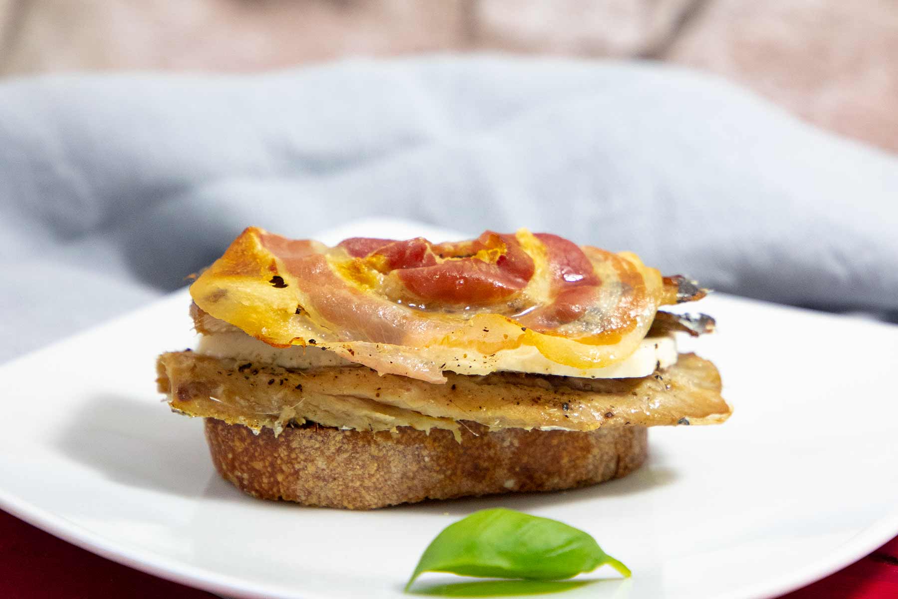 Sardinen-Bocconcini: Eine Brotscheibe belegt mit einer gegrillten Sardine, Käse und Pancetta.