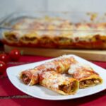 Ein Teller mit drei Cannelloni-Nudeln, gefüllt mit Fisch.