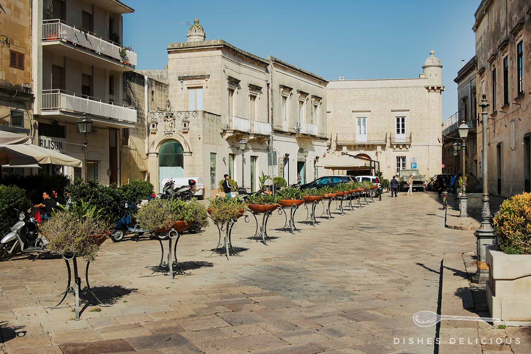 Piazza Aldo Moro mit einer langen Reihe Pflanzenkübel und alten Gebäuden.
