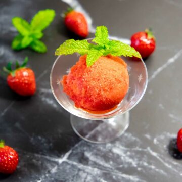 Ein kleines Schälchen mit einer Kugel Erdbeer-Sorbet, garniert mit Minzblättchen.