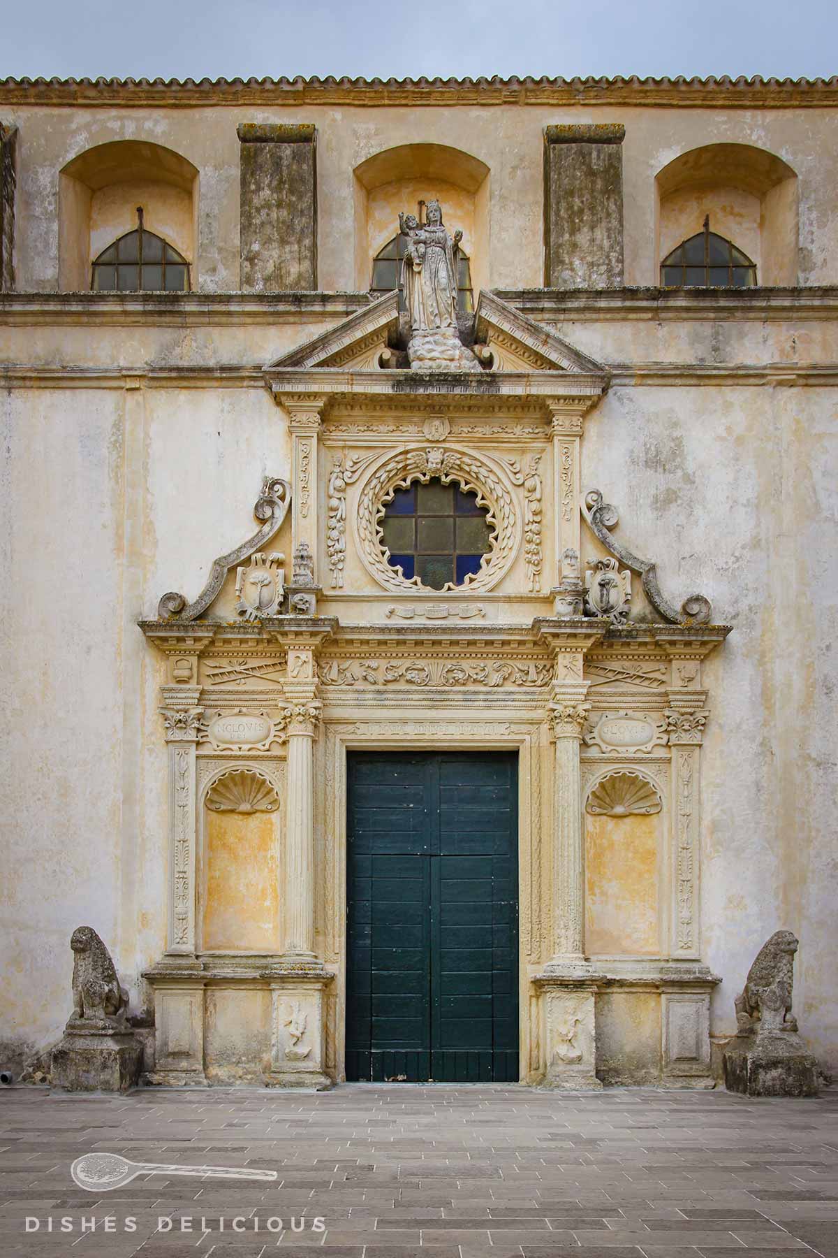 Schmuckvolles Portal der Basilica von Copertino mit verschlossenen Türen. Zwei Löwen aus Stein wachen jeweils links und rechts des Portals.