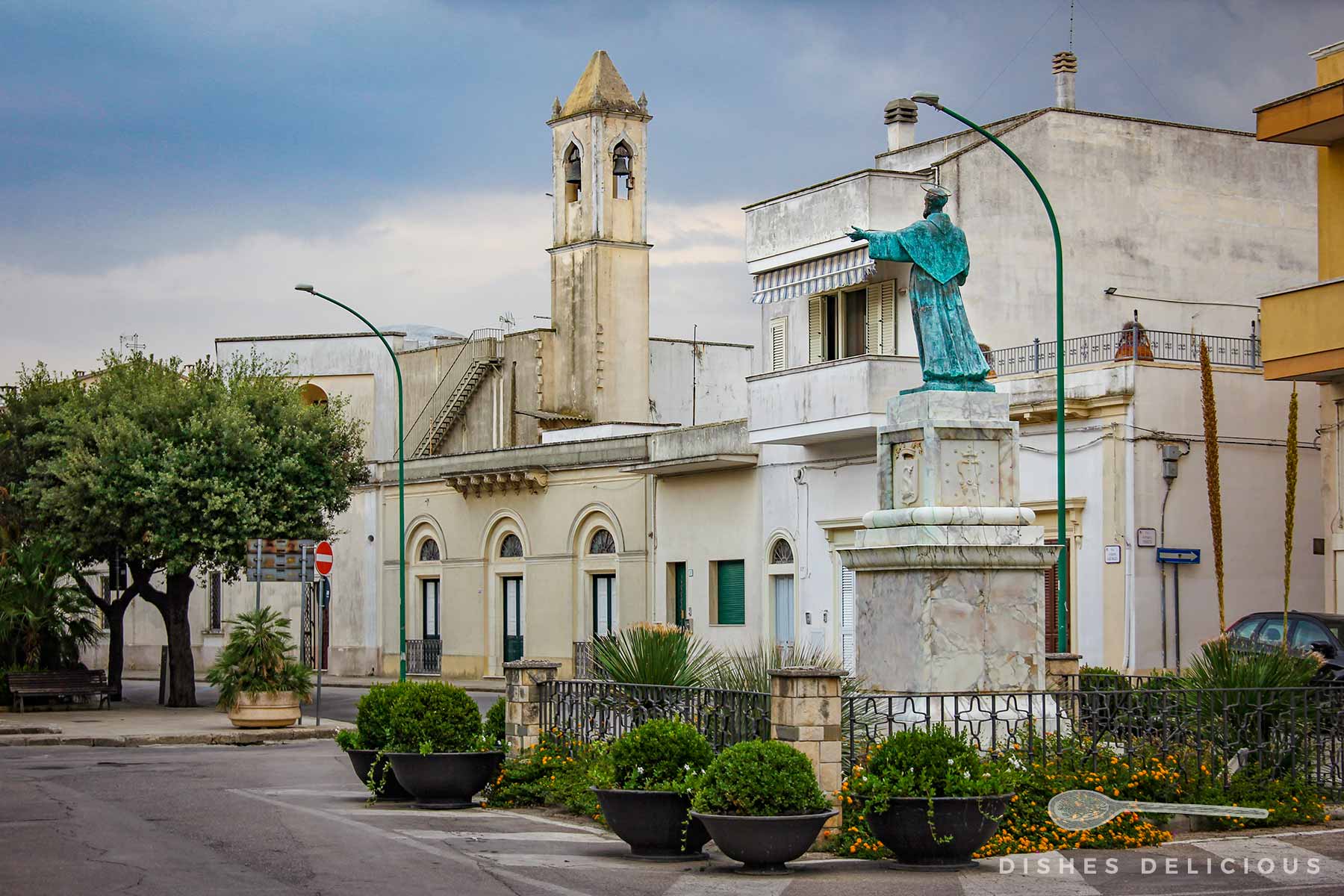 Piazza in Copertino mit einer Statue des Heiligen Josef und einem Kirchturm im Hintergrund.