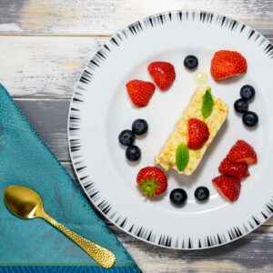 Ein Teller mit einem Streifen Mandel-Semifreddo, garniert mit Erdbeeren, Blaubeeren und zwei Minzblättchen.