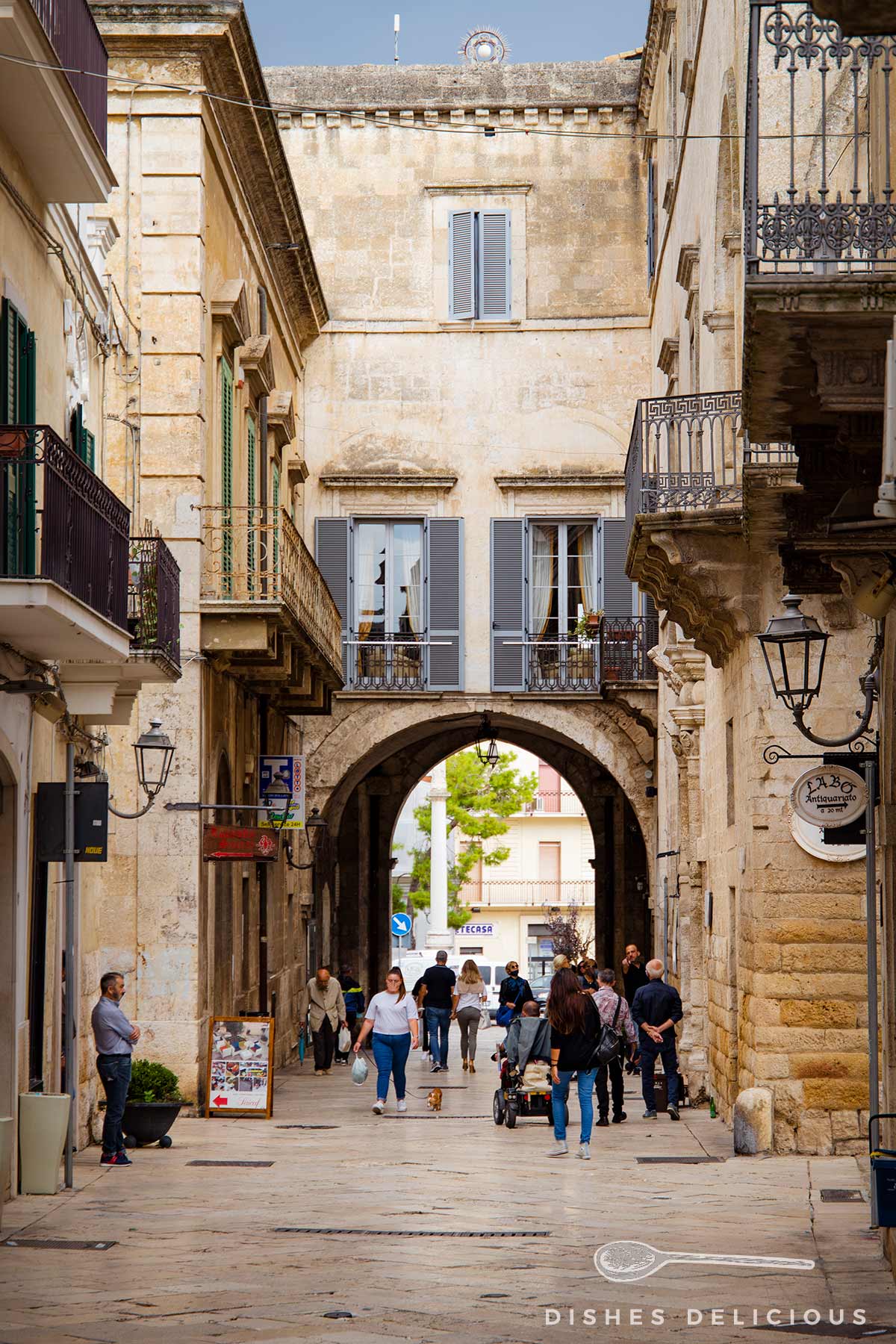Das in einen Palazzo integrierte Rundbogen-Tor Porta Bari am Ausgang der Altstadt von Altamura, Menschen laufen die Straße entlang.