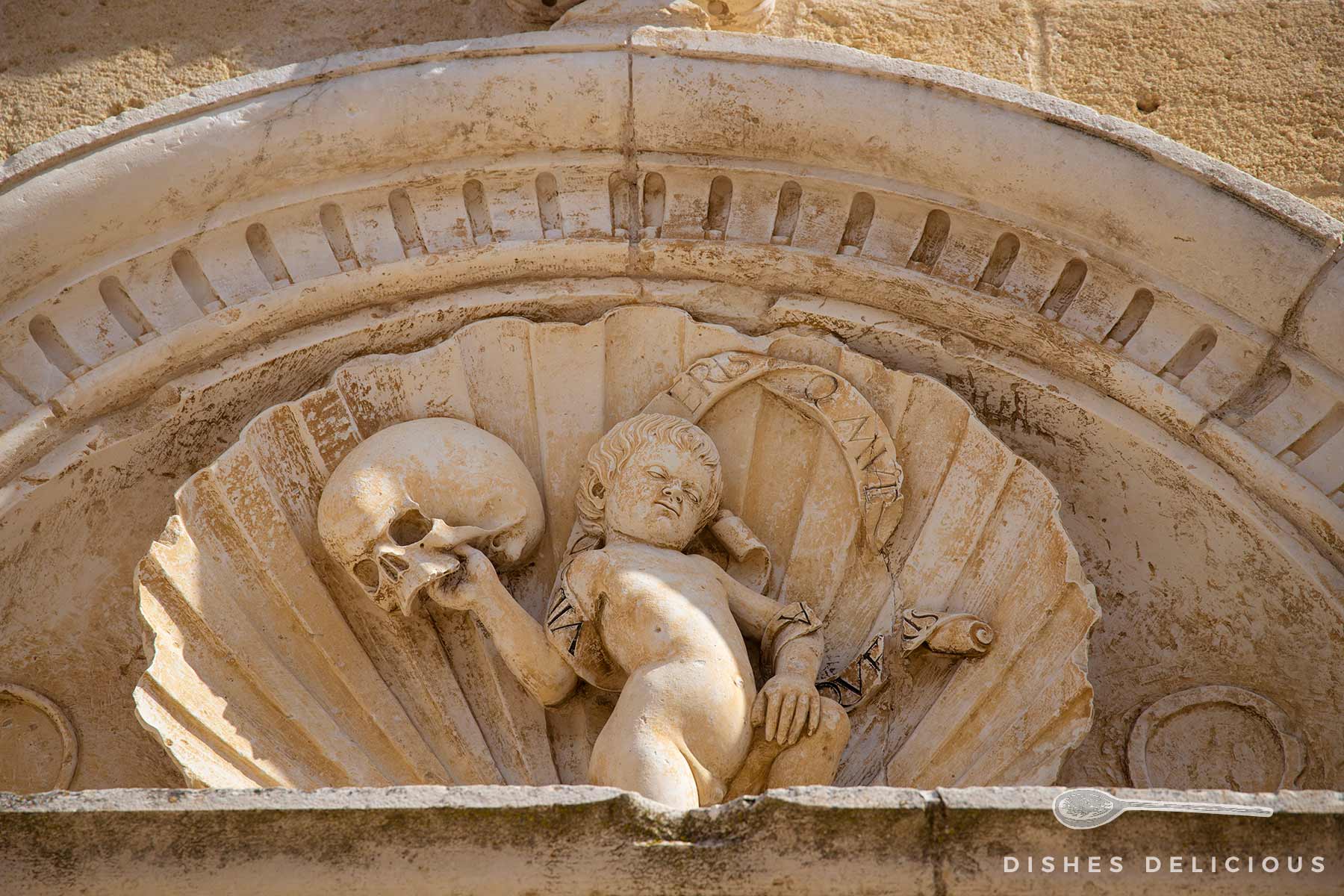Stuckverzierung einer Kirche, die einen kleinen Menschen zeigt, der in seiner rechten Hand einen großen Totenschädel trägt.