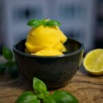 Ein Schälchen mit Mango-Sorbet, garniert mit Basilikumblättern.