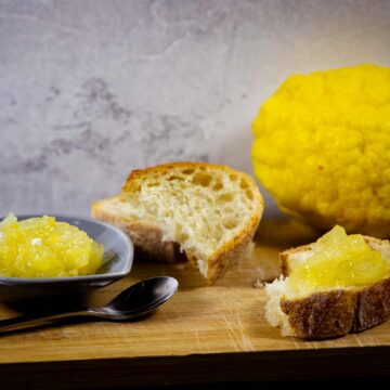 Frische Cedro-Zitronen-Marmelade auf einem Tellerchen und einer Scheibe Baguette. Im Hintergrund eine Zitronatzitrone.