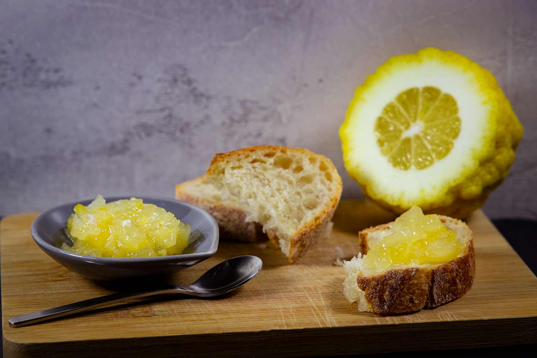 Frische Cedro-Zitronen-Marmelade auf einem Tellerchen und einer Scheibe Baguette. Im Hintergrund eine aufgeschnittene Zitronatzitrone.