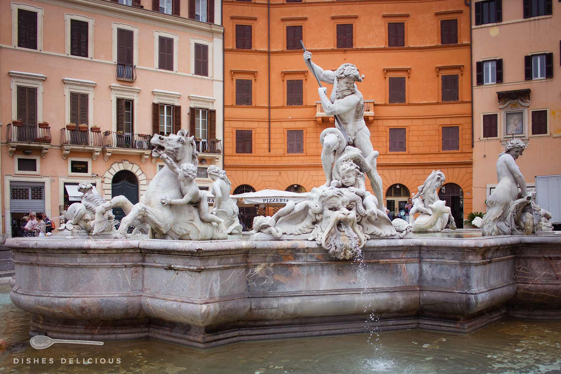 Die Brunnenfigur des Neptunbrunnens auf der Piazza Navona in Rom, umgeben von mythologischen Wesen wie Seepferden und Tritonen, vor der Kulisse historischer Gebäude mit warmen Fassaden.