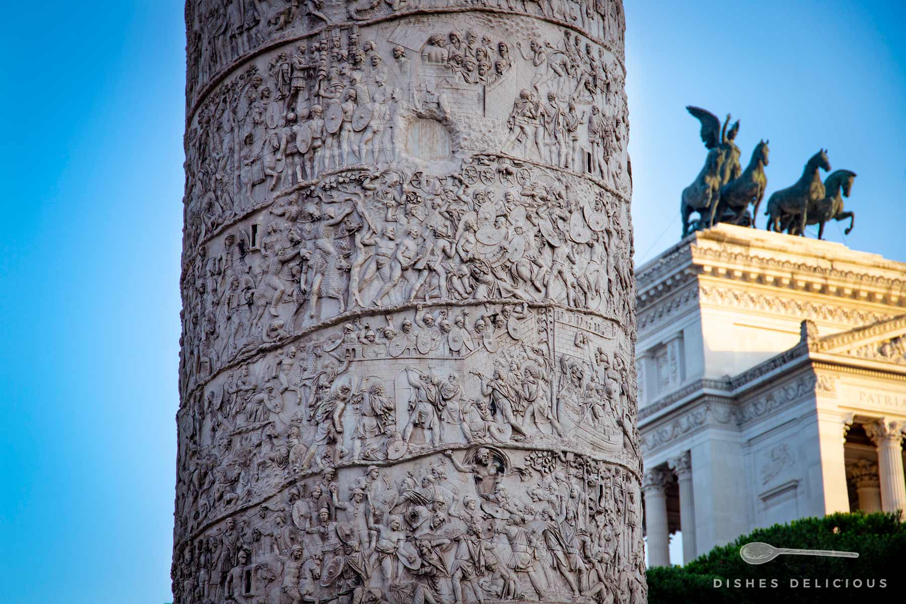 Detailaufnahme der Trajansäule in Rom mit Darstellungen der kaiserlichen Feldzüge. Im Hintergrund ist die Quadriga auf dem Vittorio-Emanuele-Denkmal zu sehen.