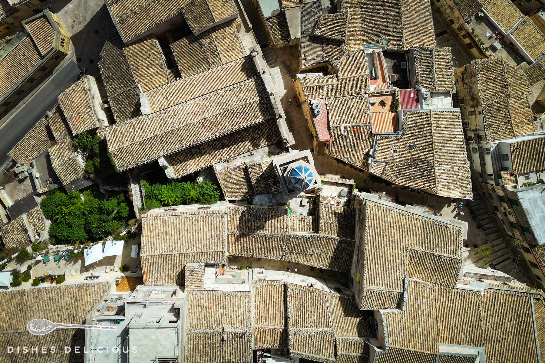 Luftschnappschuss: ein verwinkeltes Labyrinth aus terracottafarbenen Dächern, im Zentrum der Glockenturm einer Kirche.