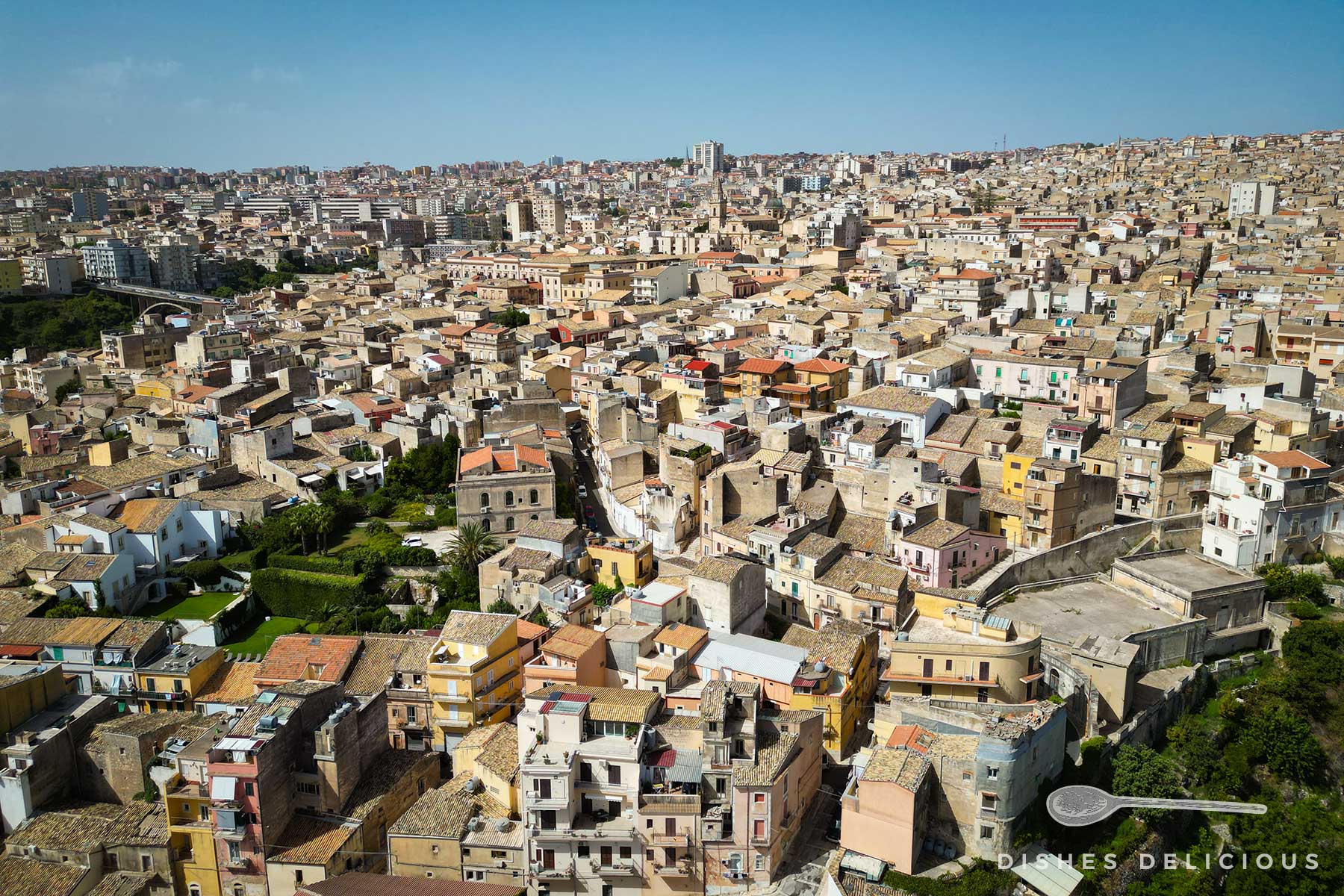 Weitläufiger Blick auf das dicht besiedelte Stadtviertel Ragusa Superiore mit vielen Häusern und Gebäuden in verschiedenen Farben und Formen.