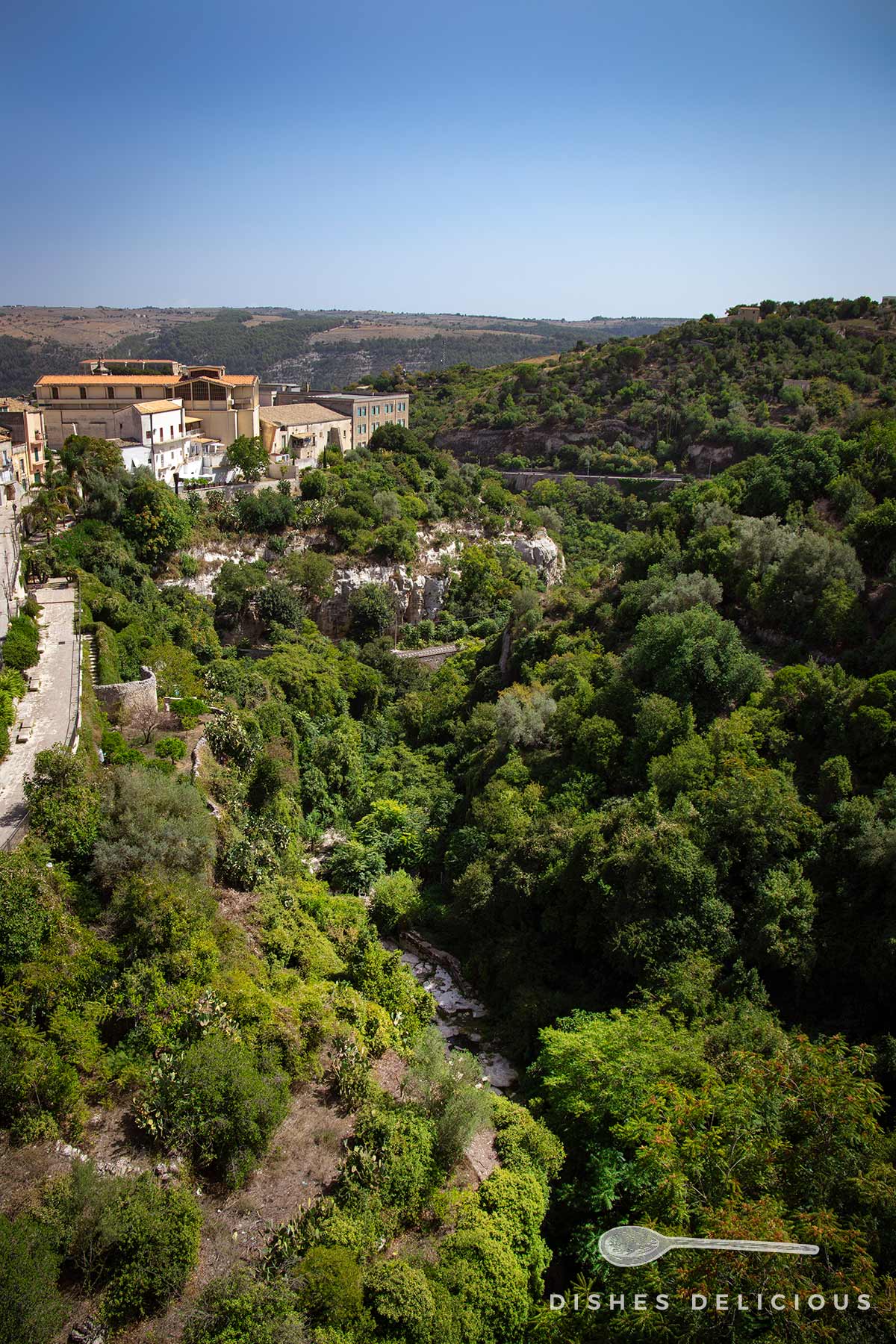 Grün bewachsenes Tal zwischen den Hügeln von Ragusa, ein kleiner Bach fließt zwischen den Bäumen und Sträuchern.