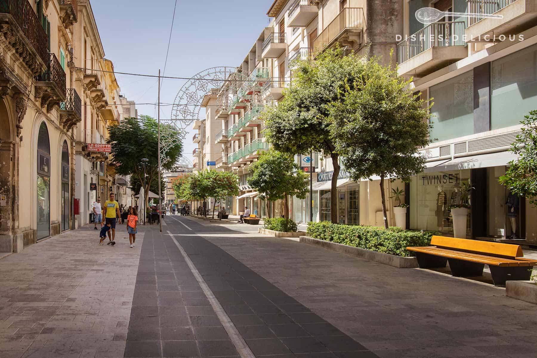 Via Roma, Ragusas elegante Einkaufsstraße, lädt mit ihren Boutiquen, Straßencafés und schattenspendenden Bäumen zum entspannten Bummeln ein.