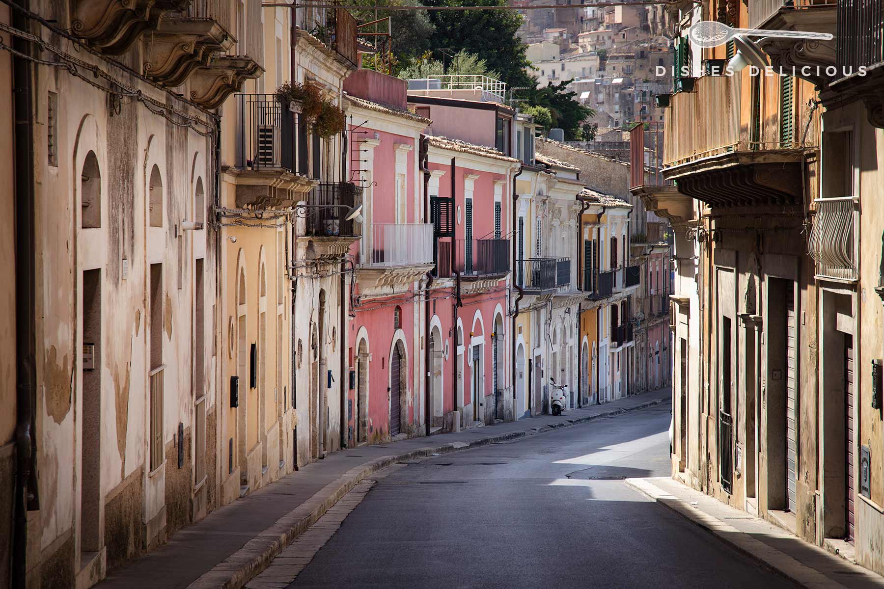 Via del Mercato in Ragusa, Sizilien, mit farbenfrohen Gebäuden. Helles Tageslicht hebt die Farben der Gebäude hervor.