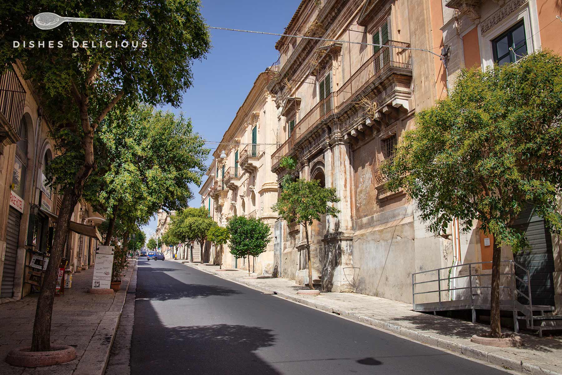 Breiten Straßen in der Oberstadt Ragusa Superiore, die von alten Palazzi und Bäumen gesäumt ist.