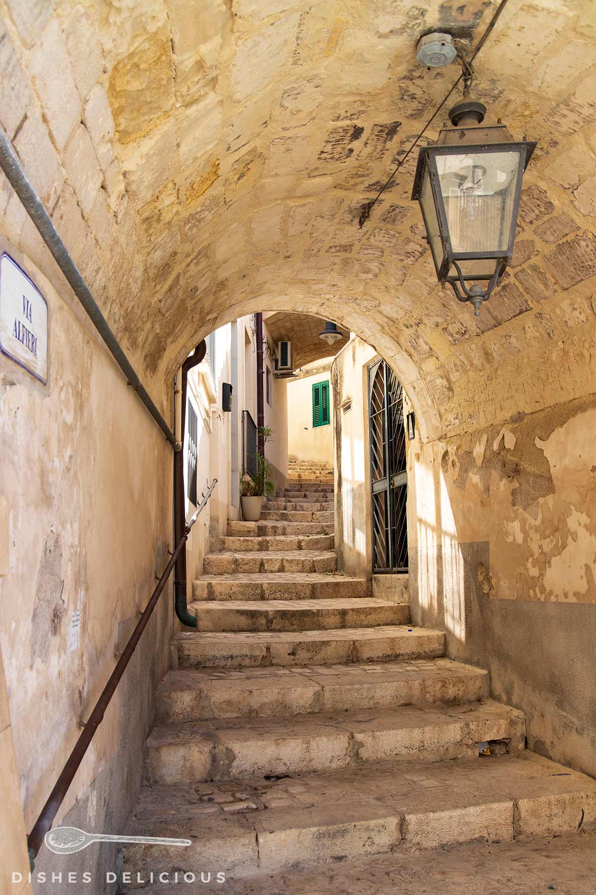 Steintreppe in einer engen Altstadtgasse, die unter einem gewölbten Bogen durchführt, an dem eine Laterne angebracht ist.