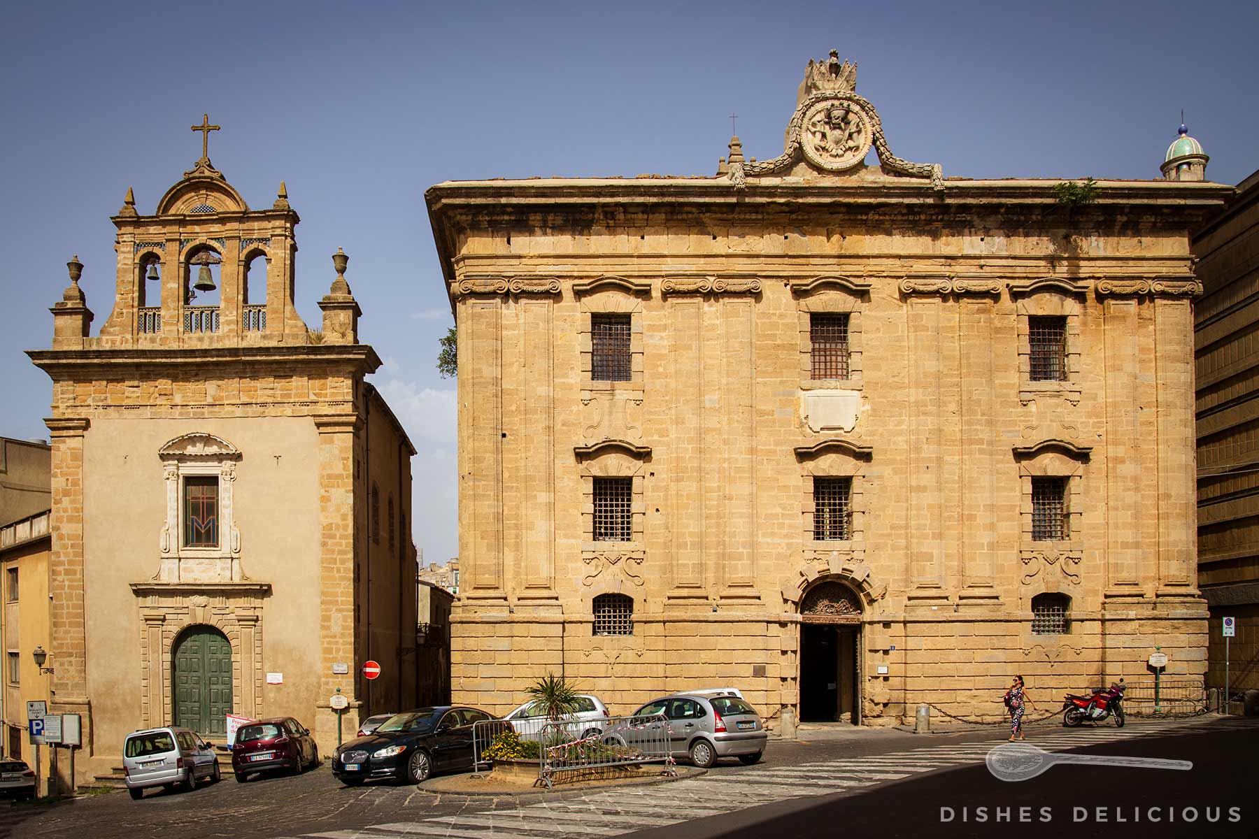 Bourbonengefängnis und Museo Civico in Caltagirone, Italien, mit parkenden Autos und einer Person auf dem Zebrastreifen.