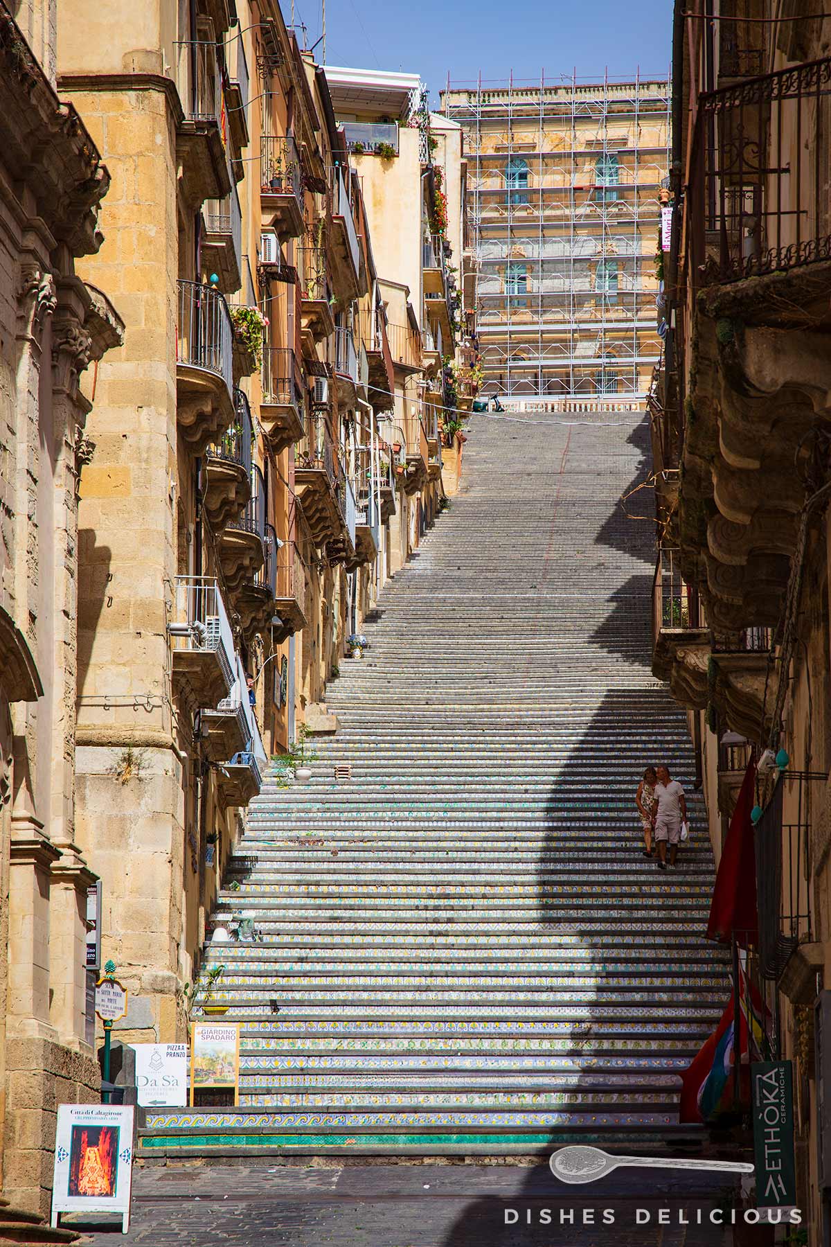 Blick auf die lange, mit bunten Kacheln verzierte Treppe Scalinata di Santa Maria del Monte in Caltagirone, flankiert von alten Gebäuden mit Balkonen.