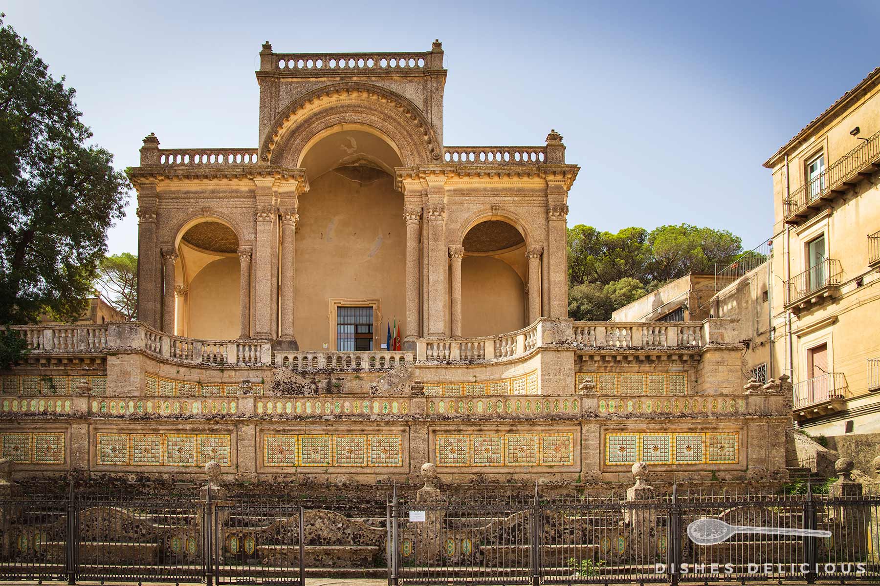 Historisches Gebäude Teatrino del Bonaiuto in Caltagirone mit dekorativen Fliesen und Säulen unter blauem Himmel.