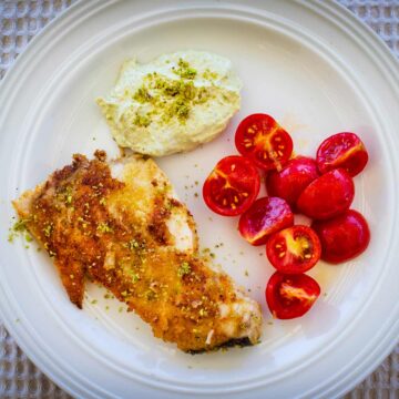 Teller mit einem gebratenen Schwertfisch in Pistazienkruste mit Kirschtomaten und einem Joghurt-Pistaziendip