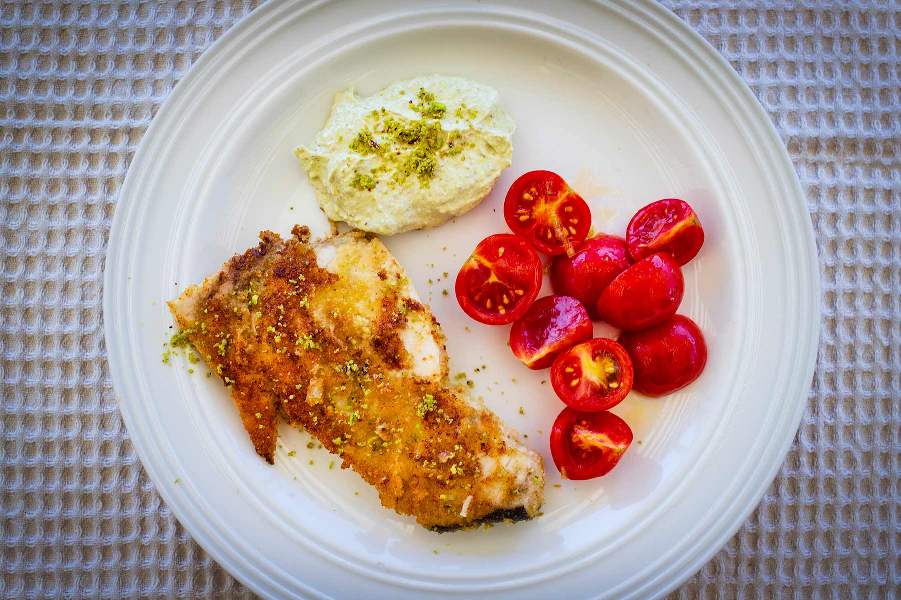 Teller mit einem gebratenen Schwertfisch in Pistazienkruste mit Kirschtomaten und einem Joghurt-Pistaziendip