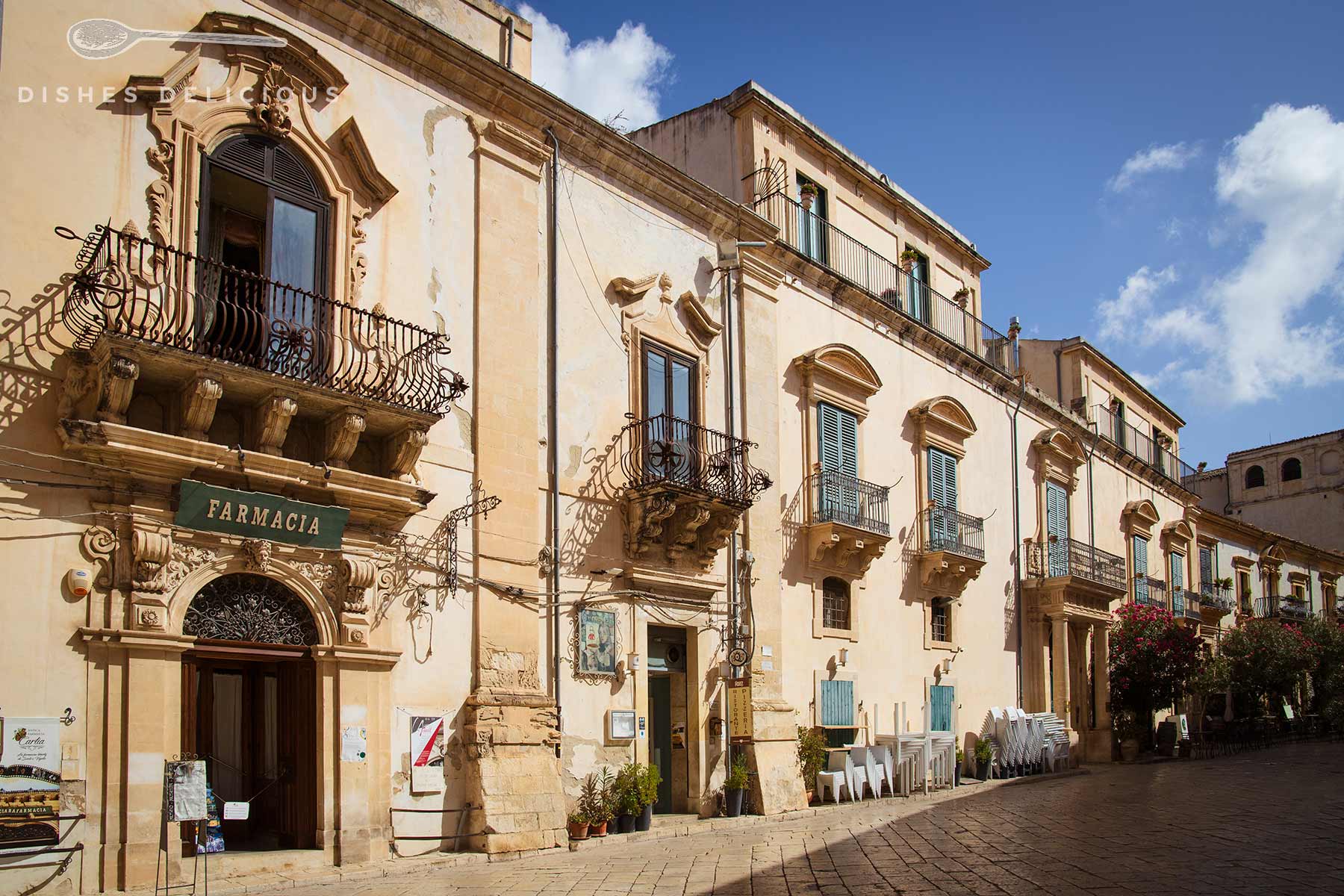 Historisches Gebäude mit barocken Balkonen und dem Schild 'Farmacia' über dem Eingang in Scicli, Sizilien.