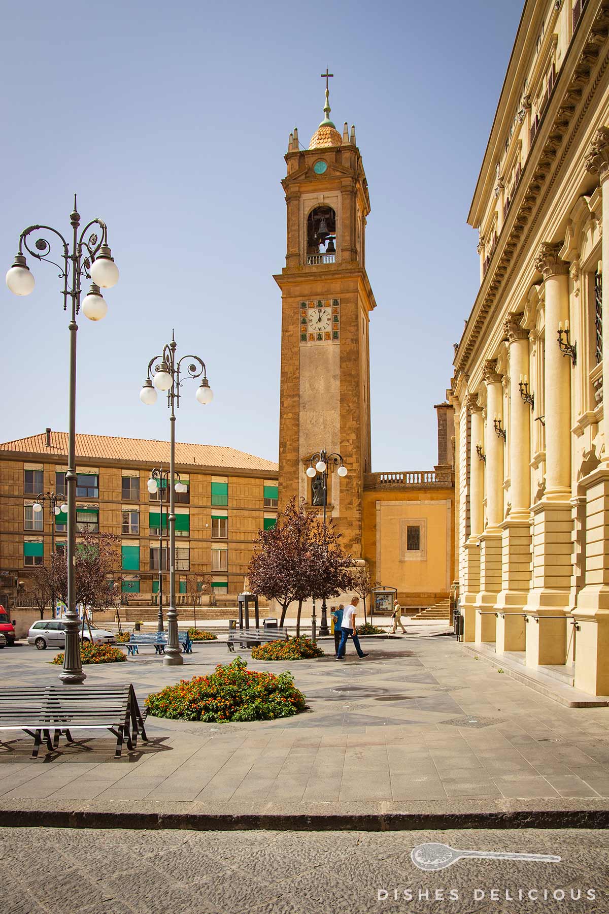 Turm der Kathedrale San Giuliano in Caltagirone, Sizilien, mit Uhr und Glocke, umgeben von Straßenlaternen und Gebäuden.