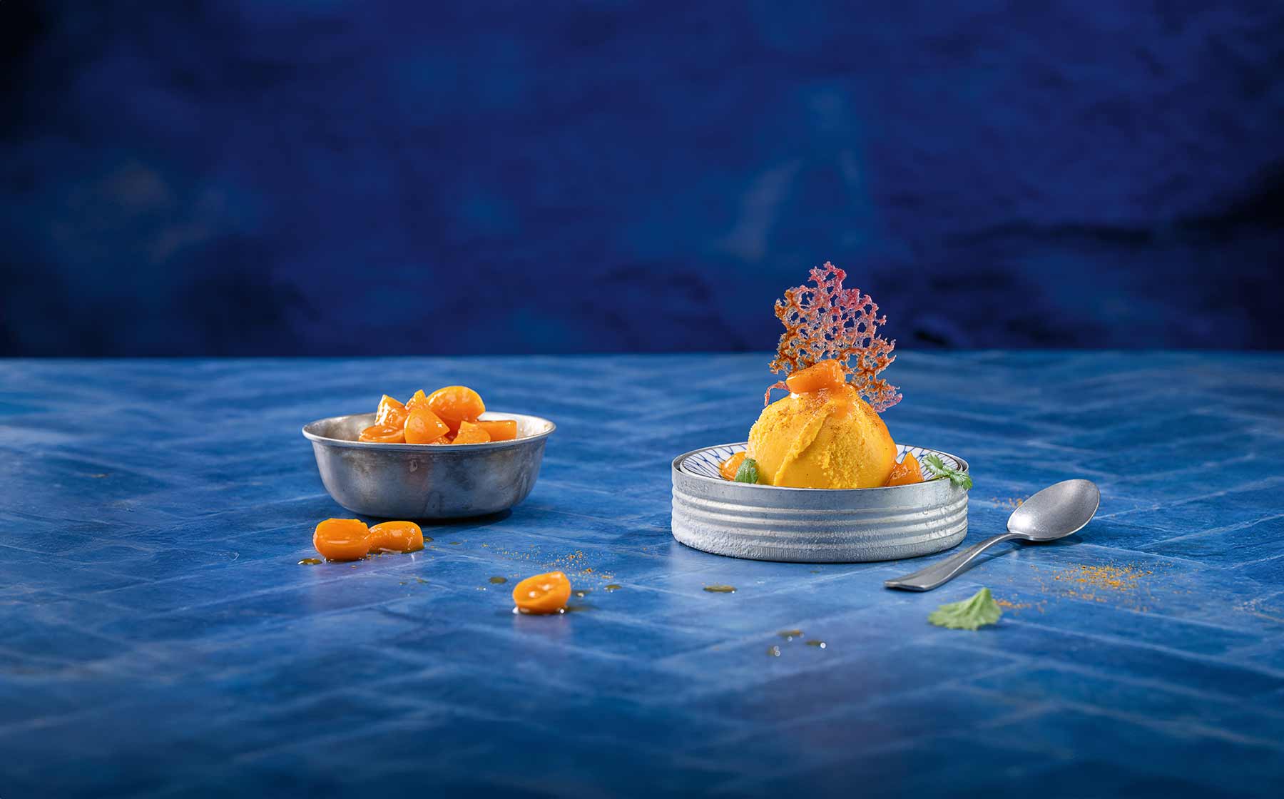 Kürbis-Curry-Eis mit Kumquats, garniert mit essbarem Dekor auf blauem Untergrund