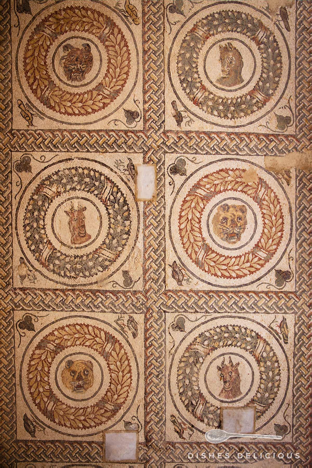 Antiker Mosaikboden mit sechs runden Medaillons, die verschiedene Tierköpfe und Figuren in der Villa Casale auf Sizilien zeigen.