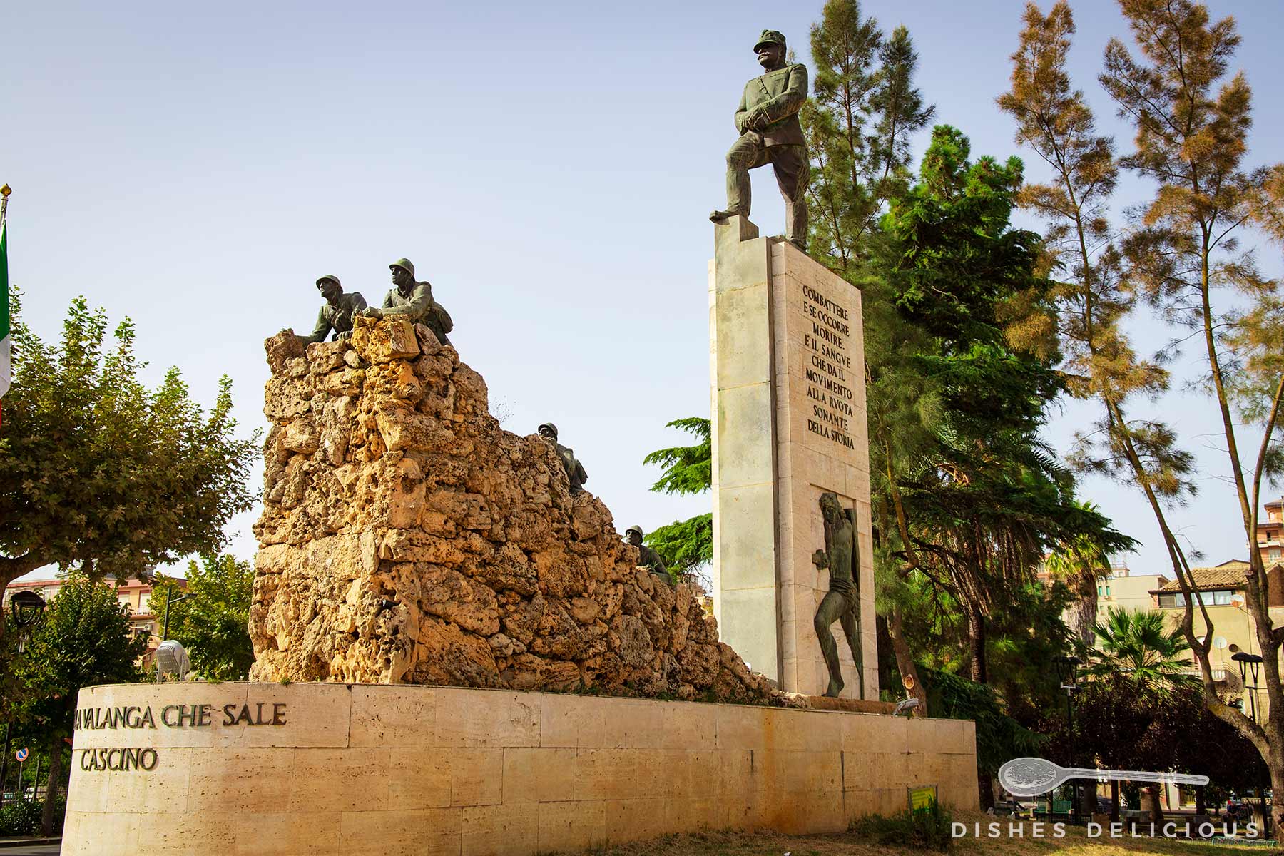 Kriegsdenkmal in Piazza Armerina mit drei Soldatenfiguren, zwei auf einem Felsen und einer auf einem hohen Sockel mit Inschrift.