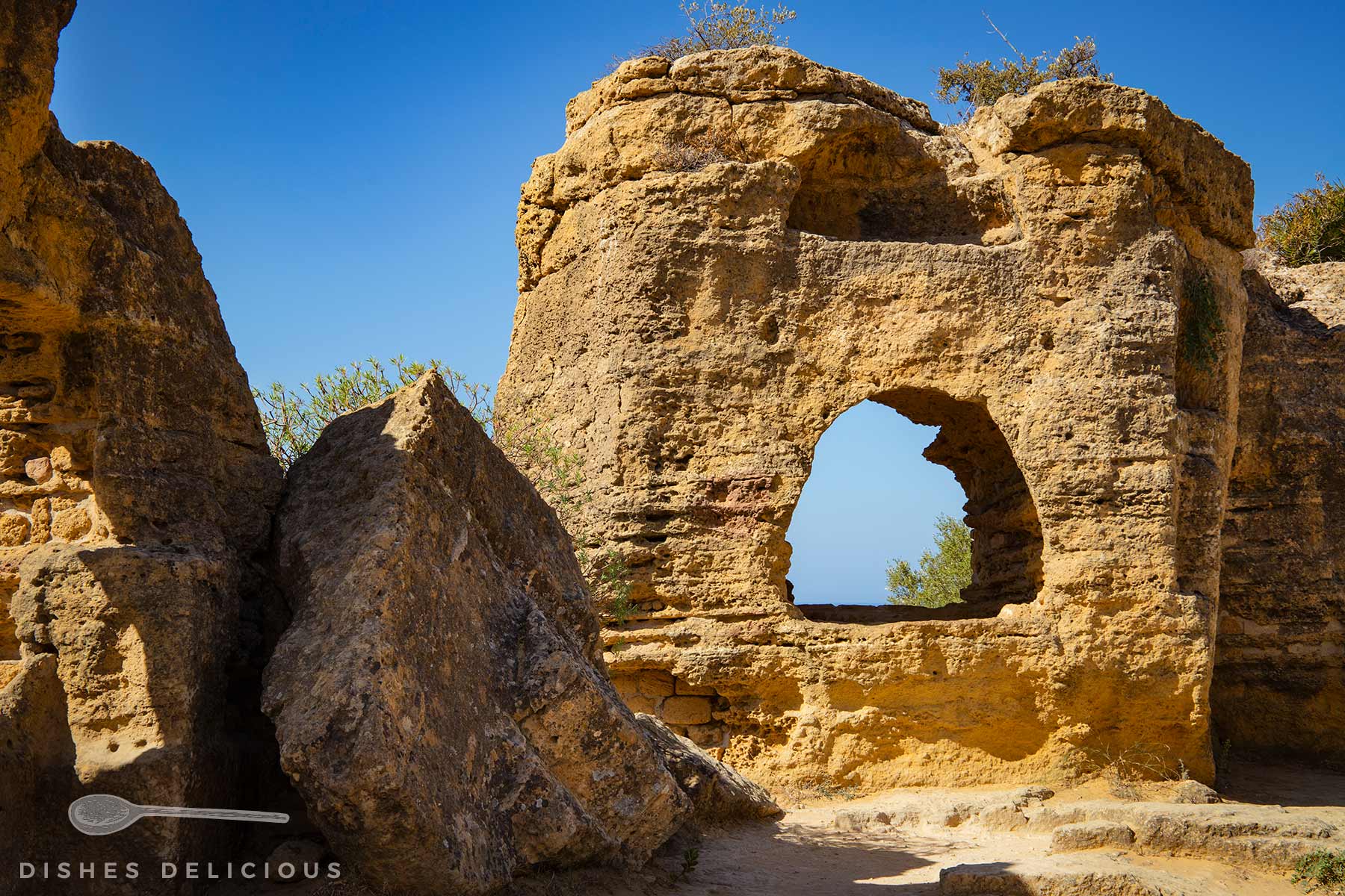Felsformation mit einem großen bogenförmigen Durchbruch im Valle dei Templi, Sizilien, unter blauem Himmel.