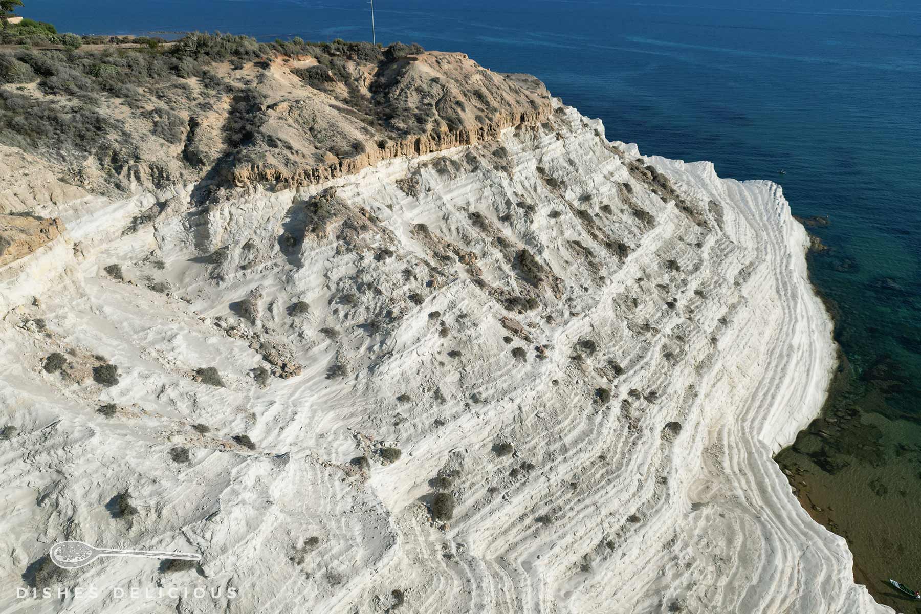 Luftaufnahme der weißen, geschichteten Kalksteinformation Scala dei Turchi mit unregelmäßigen Vertiefungen und Schatten.