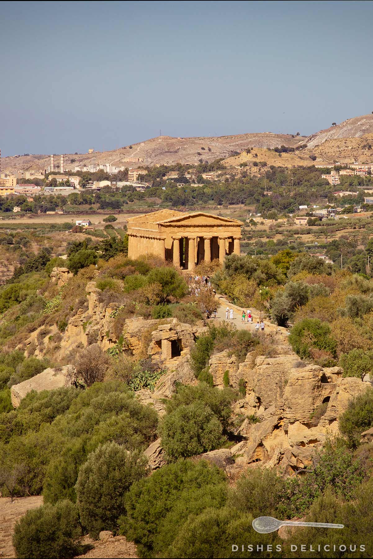Antiker griechischer Tempel mit dorischen Säulen auf einem Hügel im Tal der Tempel in Sizilien, umgeben von grüner Vegetation und Felsen.