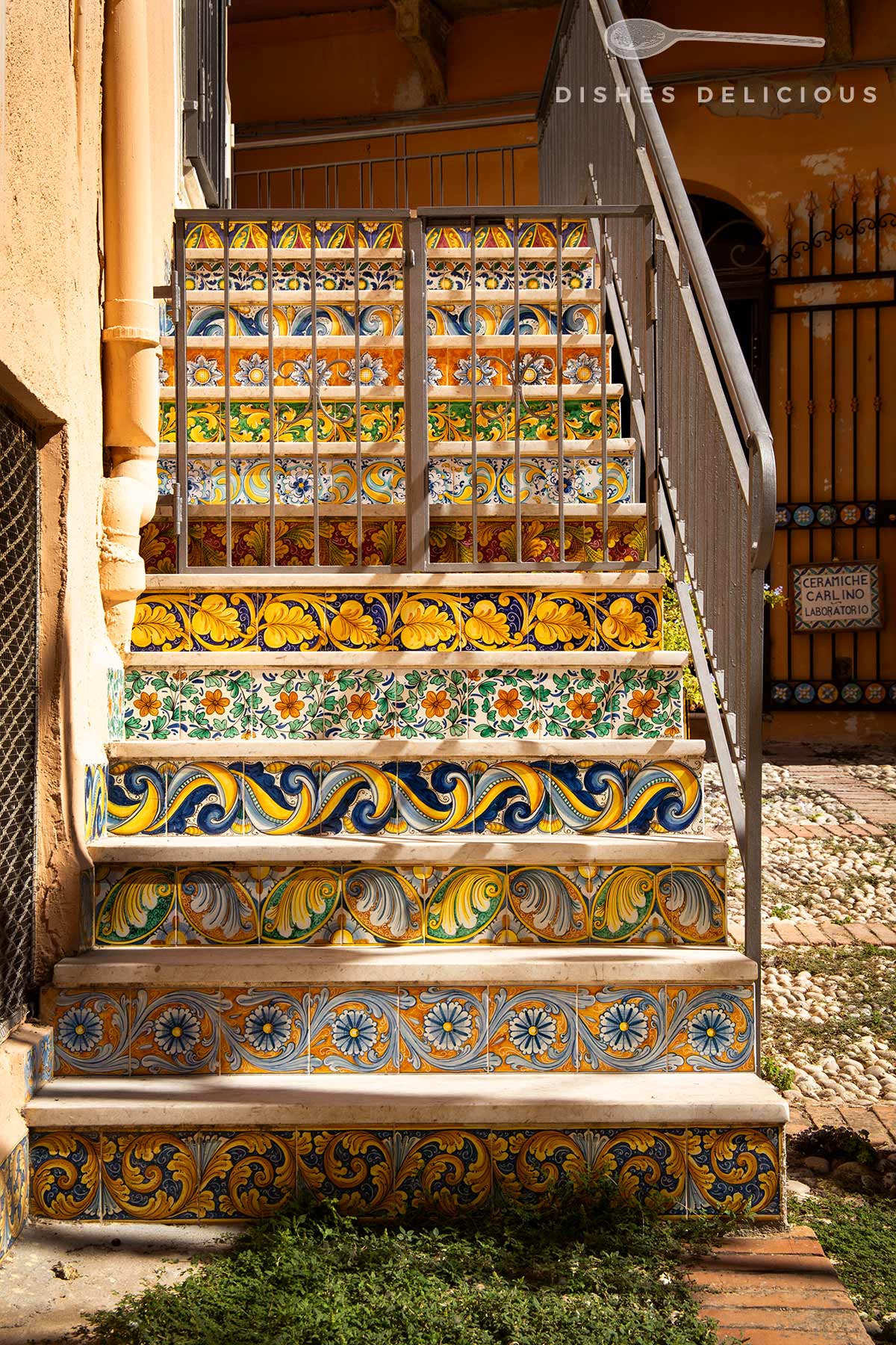 Keramiktreppe mit farbigen, floralen und ornamentalen Mustern, rechts Metallgeländer.