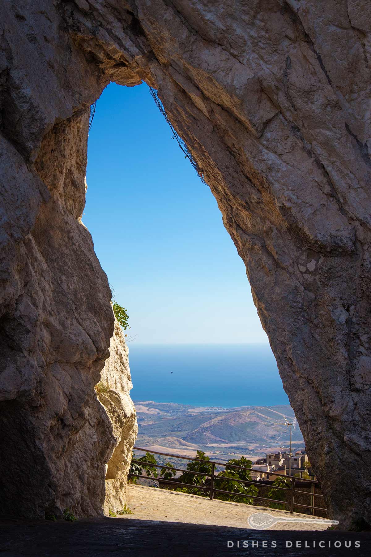Felsöffnung Lu Pirtusu mit Blick auf Landschaft, Meer und Dorf unter blauem Himmel in Caltabellotta, Sizilien.