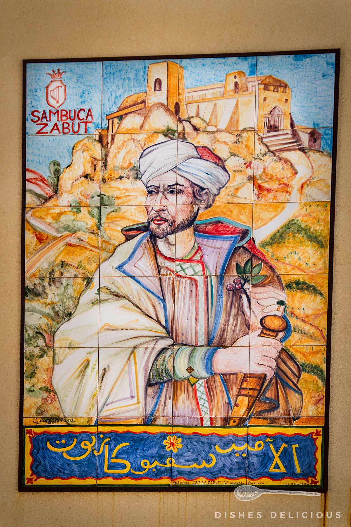 Wandbild mit einem Sarazenen in traditioneller Kleidung vor einer Landschaft mit Burg und Felsen, Schriftzug 'Sambuca Zabut' und arabische Schriftzeichen am unteren Rand.