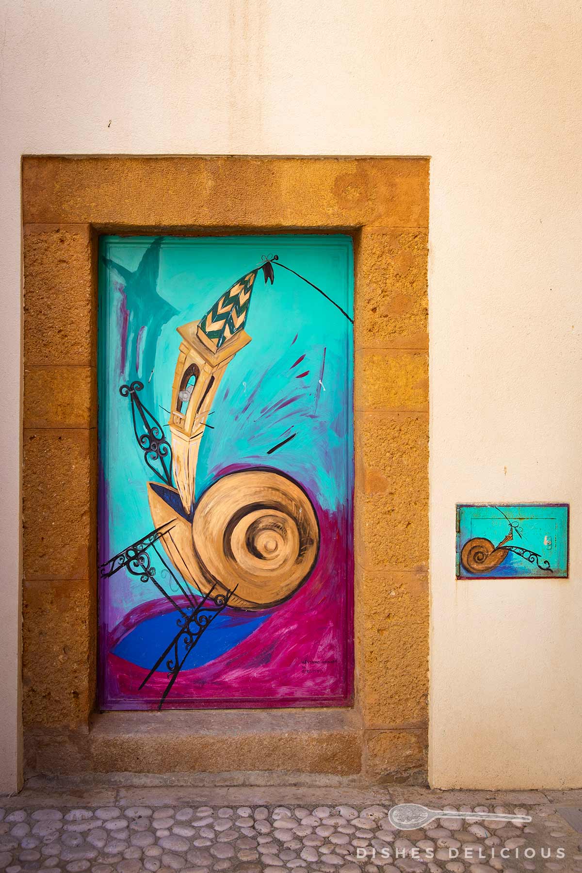 Bunte Wandmalerei mit abstraktem Turm und Spirale in einem steinernen Türrahmen, daneben kleines Bild mit ähnlichem Motiv an weißer Wand.