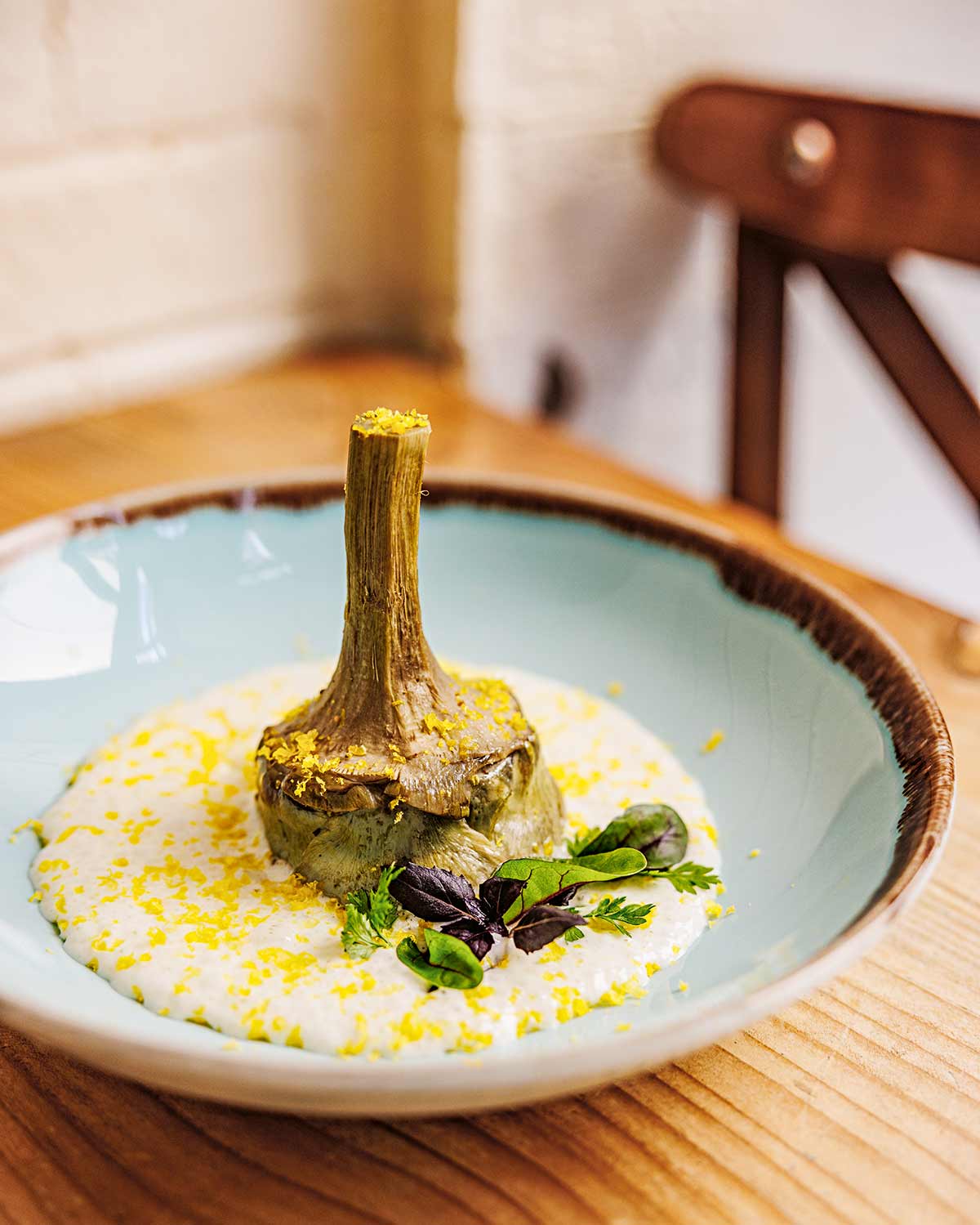 Ganze Artischocke mit Stiel steht auf cremiger Sauce, garniert mit Kräutern auf hellem Teller.