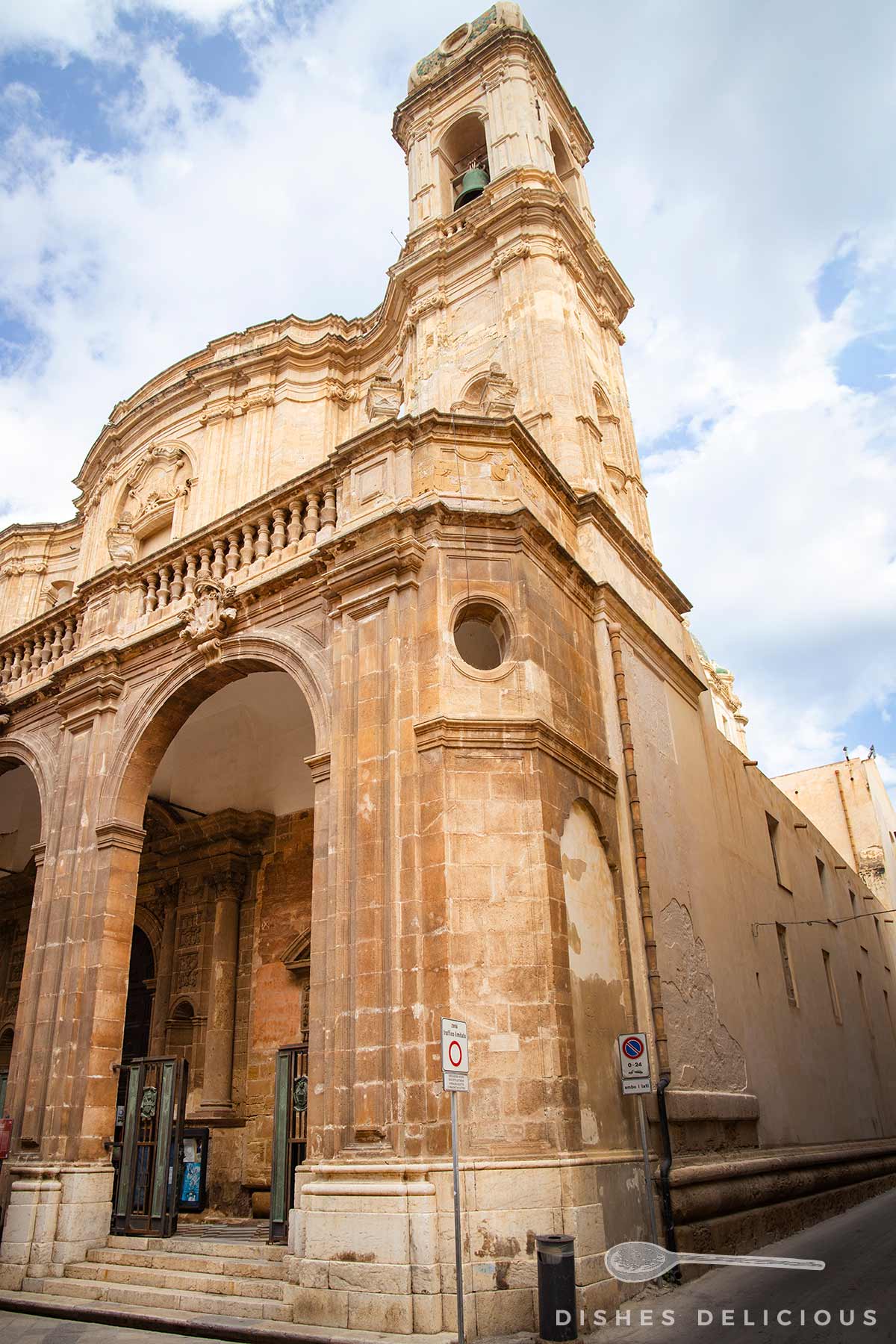 Nahaufnahme der Cattedrale San Lorenzo in Trapani mit Säulen, Rundbogen und einem Turm unter bewölktem Himmel.