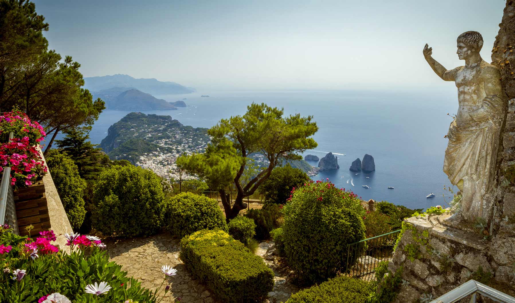 Blick über Capri und das Meer vom Monte Solaro aus. Im Vordergrund ein Garten und eine Statue.